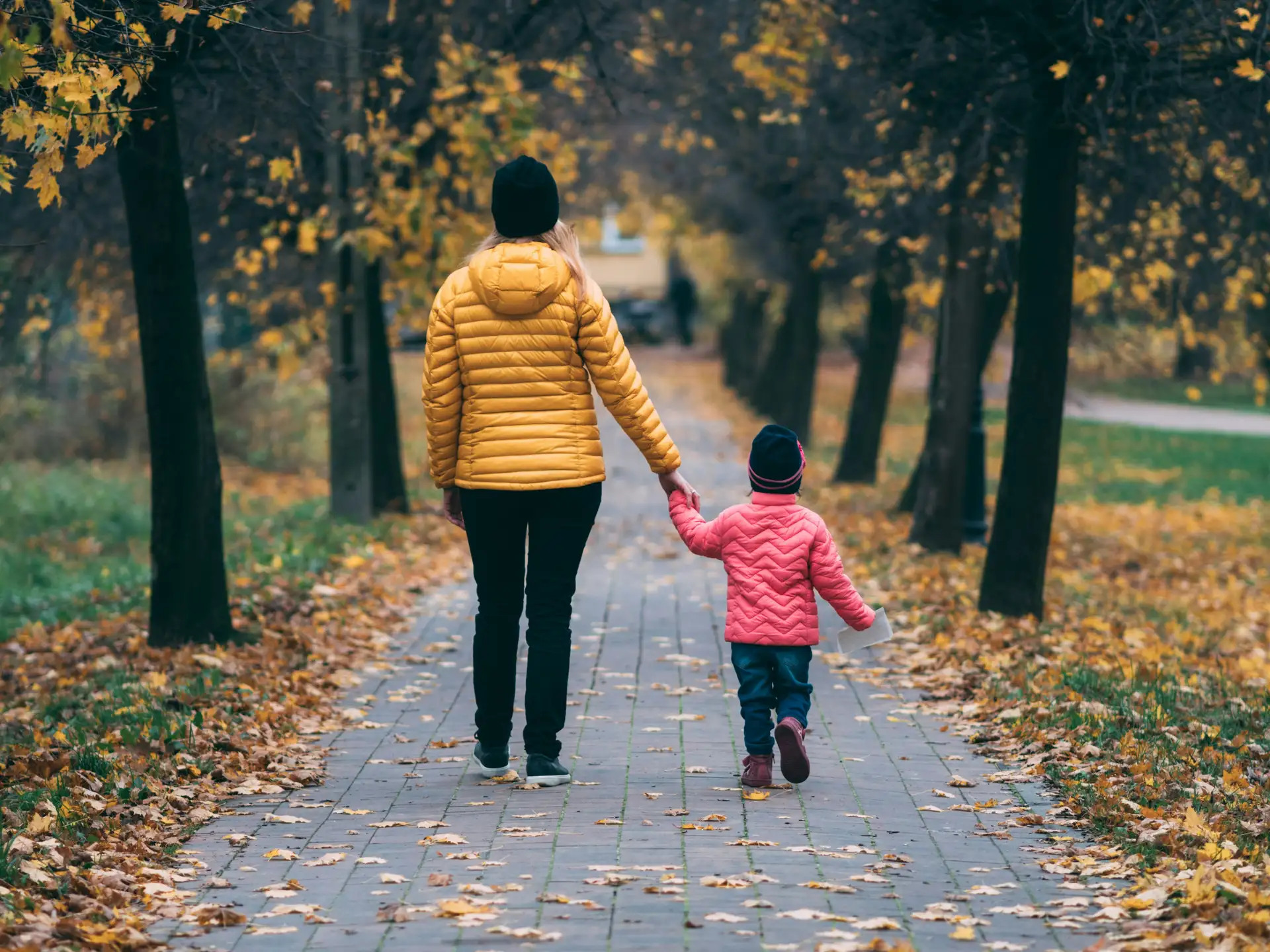 Moeder en jong kind die hand in hand over een herfstig parkpad wandelen